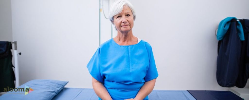 כירורג שד במרכז
 - ניתן לראות אישה מבוגרת עם שיער לבן ולבושה בחלוק מטופלים ובצד שמאל למטה לוגו אתר alooma